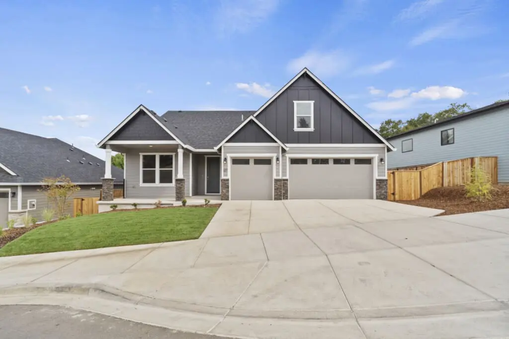 Discover a modern single-story house on 1343 N Kalani Loop, featuring dark gray siding, white trim, and a double garage. Enjoy the well-maintained front lawn and wide driveway. The sky above this Paradise 53 residence is clear with a few clouds.