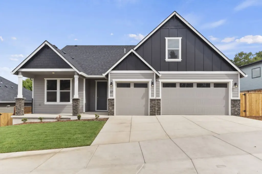 A modern two-story house on N Kalani Loop features gray siding and a large driveway with a well-maintained lawn. This Paradise 53 home boasts a double garage, a covered front porch, and triangular roof peaks set against a pristine blue sky.