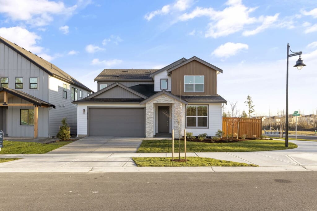 Nestled on Eagle Ln in Tehaleh, this modern two-story house features a stone facade, gray and white color scheme, and a two-car garage. The neatly landscaped front yard with its wooden fence sits under a clear blue sky, with a streetlamp visible on the right. Home sweet 20310.