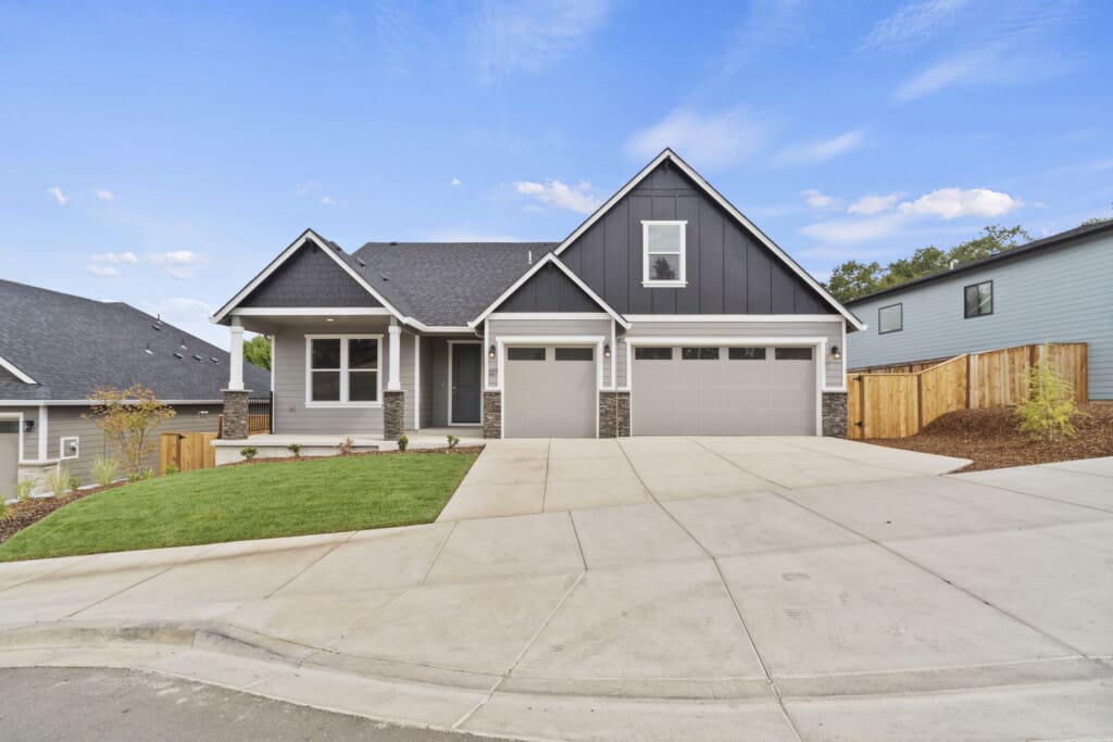 Discover a modern single-story house on 1343 N Kalani Loop, featuring dark gray siding, white trim, and a double garage. Enjoy the well-maintained front lawn and wide driveway. The sky above this Paradise 53 residence is clear with a few clouds.