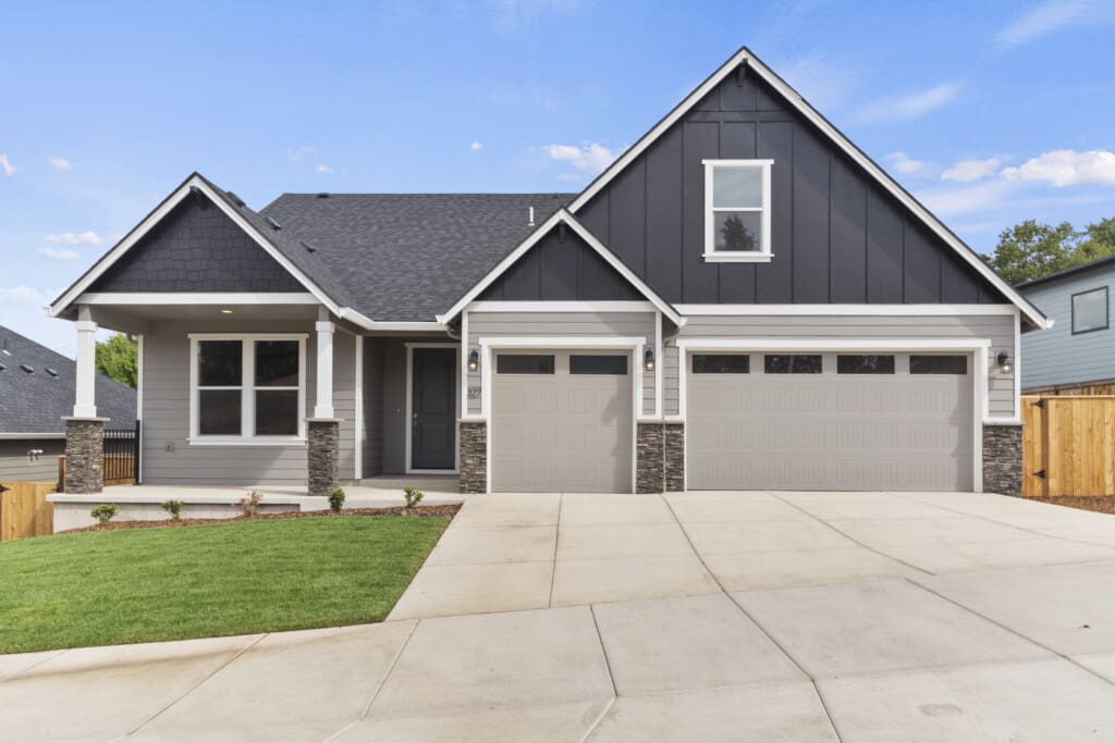 A modern two-story house on N Kalani Loop features gray siding and a large driveway with a well-maintained lawn. This Paradise 53 home boasts a double garage, a covered front porch, and triangular roof peaks set against a pristine blue sky.