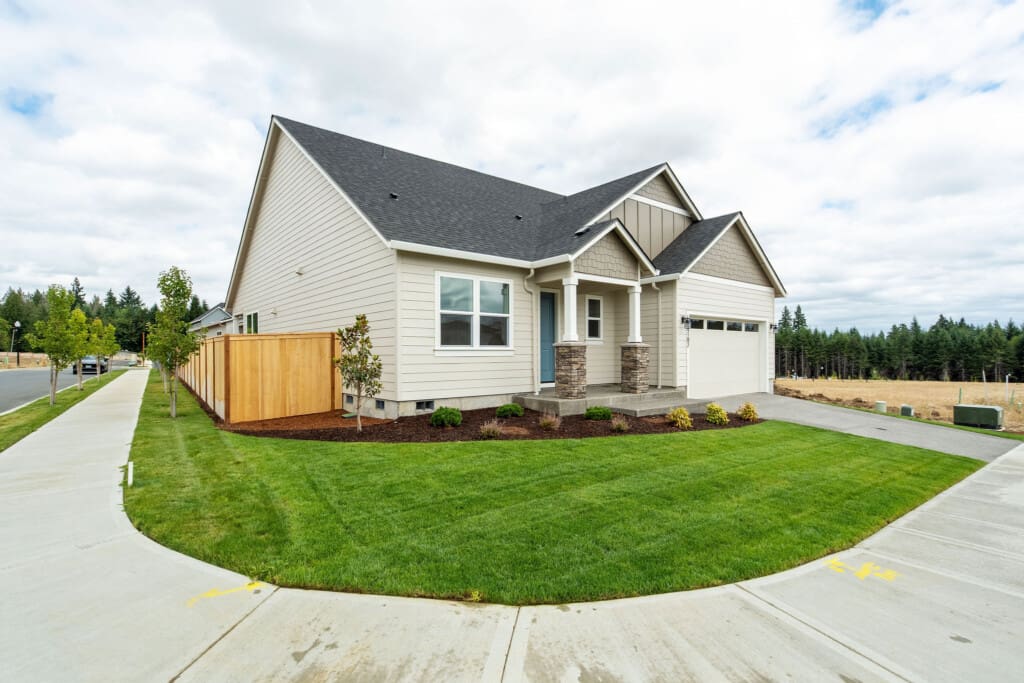 Charming single-story Ramble Creek home at 4102 NE 187th St with light siding, dark roof, a front porch with stone pillars, double garage, and manicured lawn on a corner lot, bordered by a wooden fence and sidewalks.
