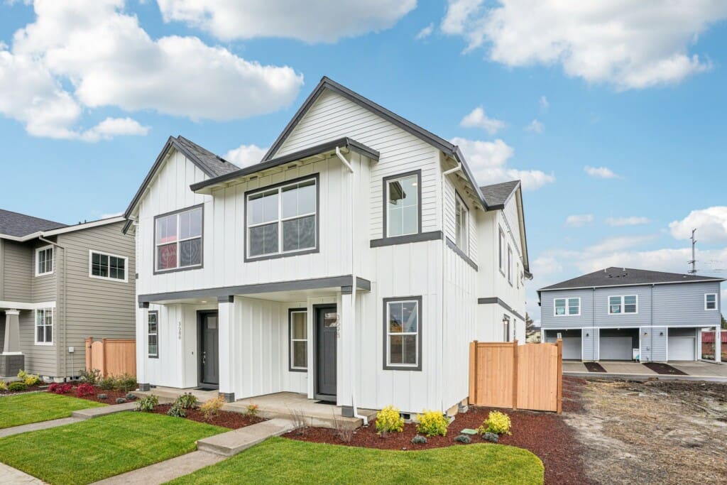 A modern two-story white house with black trim at 3586 SE 86th Ave, featuring large windows and a small front garden in Reed's Crossing. The suburban property has a fenced backyard, driveway, and sits under a partly cloudy sky.