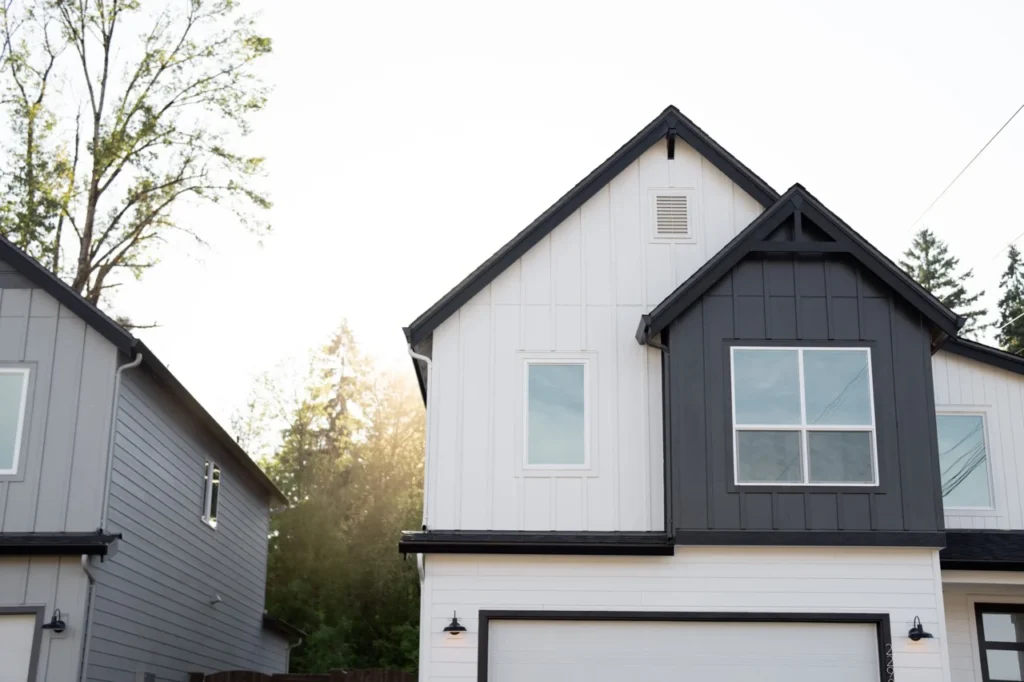A modern two-story house with white and dark gray siding, large windows, and a double garage. Sunlight shines through trees in the background, perfect for featuring a finance offer on your real estate landing page.
