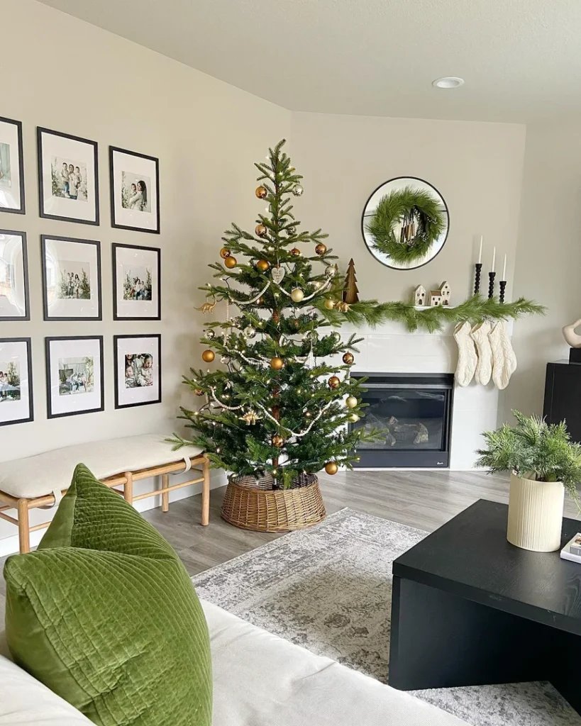A decorated Christmas tree stands beside a fireplace with stockings, candles, and seasonal decor. Family photos hang on the wall, and a green pillow is on a white sofa in this cozy, modern living room ready to decorate for the holidays.
