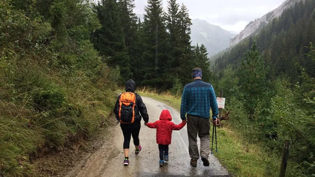 Three people, two adults and a child in a red coat, walk hand-in-hand along a forested mountain path near Estacada Oregon. Surrounded by tall trees and misty mountains, they explore the scenic trails of Faraday Hills together.