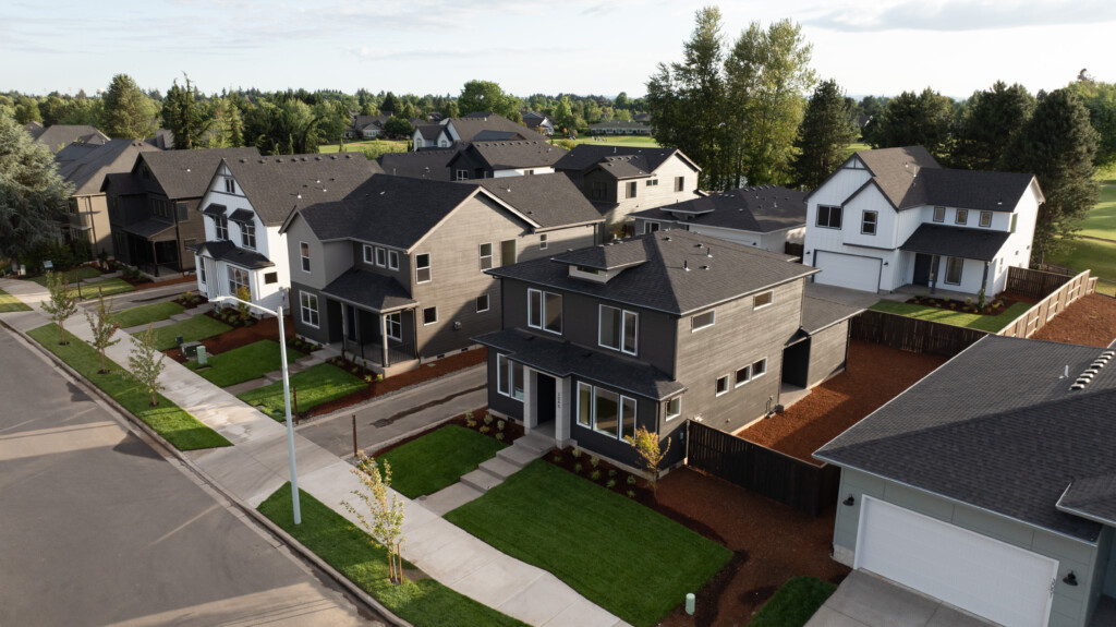 Aerial view of a new construction community with modern, two-story houses, green lawns, sidewalks, and young trees along quiet streets—ideal for those seeking buying advice on sought-after features in suburban living.