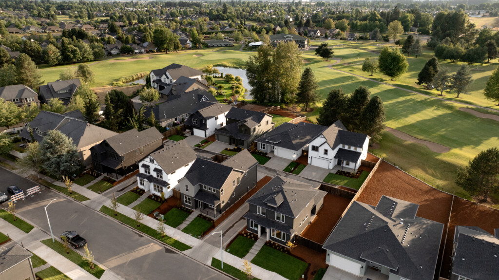 Aerial view of a suburban home community with rows of modern houses, green lawns, trees, and winding pathways along a golf course under a clear sky—showcasing what to expect from new construction homes in the area.