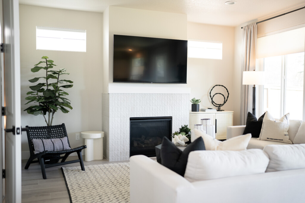 Experience modern living in the Creekside Heights new model: a stylish living room with white walls, sleek furnishings, a large TV above the fireplace, and ample natural light streaming through the windows at 2366.