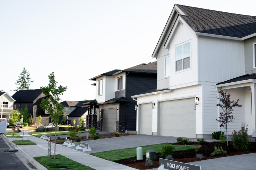 A row of modern, two-story suburban houses with well-kept lawns and young trees lines a clean sidewalk under a clear sky—an inviting scene for those ready to explore mortgage benefits when they work with a lender.